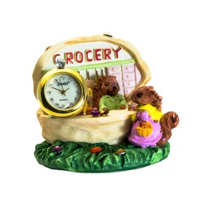 May include: A miniature grocery store figurine with a clock face and two squirrels. The store is made of ceramic and painted in bright colours. The sign above the store says "GROCERY".