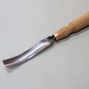 May include: A curved wood carving tool with a metal blade and a wooden handle. The handle is made of light brown wood and has a copper ferrule.