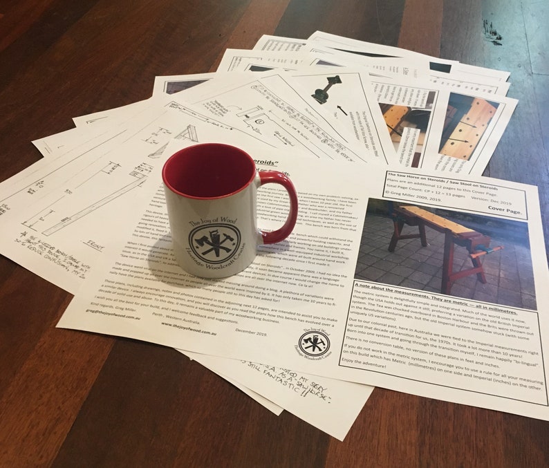 May include: A red and white mug with a logo that says "The Joy of Wood" and a crossed axe design. The mug is sitting on a table with a stack of papers. The papers are blueprints for a woodworking project. The text on the papers says "The Low Stove on Stands / Raw Stand on Stands".