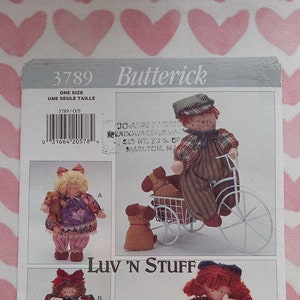 May include: A sewing pattern for making dolls, including a girl with a bicycle, a girl with a teddy bear, a girl with a gift, a girl with kittens, and two angels. The pattern is from Butterick and is called "Luv 'N Stuff".