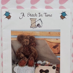 May include: A sewing pattern for a brown teddy bear named Benjamin Bear. The pattern includes a picture of a finished teddy bear sitting on a crocheted doily with a pillow featuring a smaller version of the bear.