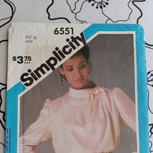 May include: Simplicity sewing pattern number 6551 for a blouse with a high neck and a bow tie. The pattern is for size 16 miss and costs $3.75. The pattern includes three different views of the blouse.