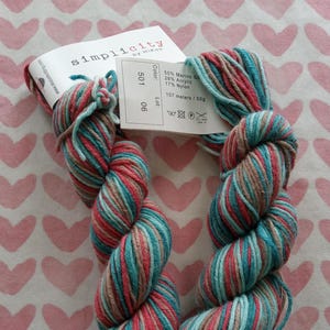 May include: Two skeins of Simplicity yarn by Hiko, in a colorway of teal, red, and tan stripes. The label indicates the yarn is 55% Merino wool, 28% acrylic, and 17% nylon. Each skein contains 107 meters of yarn, or 50 grams.