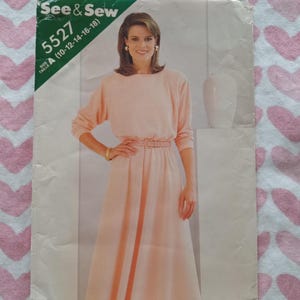May include: A vintage sewing pattern from See & Sew, featuring a woman in a light pink dress with a belted waist and long sleeves. The pattern number is 5527, with size options A (10-12-14-16-18). The words "PATTERN/PATRON" are printed at the bottom.