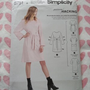May include: Simplicity pattern 8751 A. The pattern features a woman wearing a light pink dress with a belt. The pattern includes options for a drawstring waist, flounce sleeves, and an origami elbow sleeve. The text on the pattern reads "HACKING".