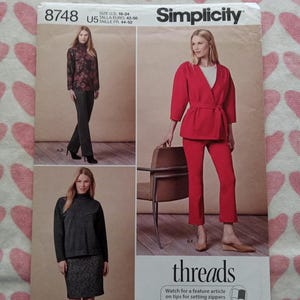 May include: Simplicity sewing pattern 8748 featuring three different outfit options. The pattern includes a red pantsuit, a black and gray skirt suit, and a floral top with black pants. The pattern size is U.S. 16-24.