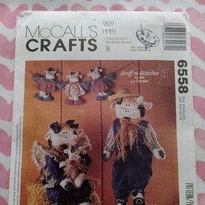 May include: A sewing pattern for a family of three cow-themed stuffed toys. The pattern is called "Stuff-n-Stitches" by Liz Hansen. The pattern includes instructions for making a mom cow, a dad cow, and a baby cow. The cows are all dressed in plaid shirts and denim pants. The pattern also includes instructions for making a cow garland.