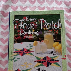 May include: A book titled "Easy Four-Patch Quilting" with a green border. The cover features a quilt design with red, blue, and yellow star patterns, and a pitcher of lemonade with lemons. The book is by House of White Birches.