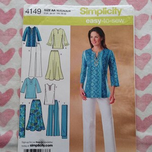 May include: A Simplicity easy-to-sew pattern, size AA 10,12,14,16,18, featuring a woman in a blue tunic and white pants. The pattern includes illustrations of various tops, skirts, and pants. The background is a pink and white heart pattern.