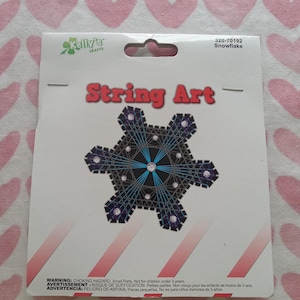 May include: A String Art kit by Kelly's Crafts, featuring a snowflake design. The kit includes a black and blue snowflake pattern with a central starburst design. The package has the text "String Art" in red.