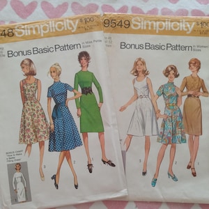 May include: Two vintage Simplicity sewing pattern envelopes. The envelopes feature illustrations of women in dresses. The text on the envelopes reads "9548" and "9549" with "Bonus Basic Pattern" and "$1.00" printed on them.