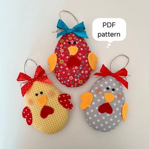 Puede incluir: Tres adornos de pollitos de Pascua hechos a mano de fieltro con diferentes patrones. Los pollitos son rojos, amarillos y grises con lunares blancos. Cada pollito tiene un lazo y una cuerda para colgar. El texto "Patrón PDF" está en un bocadillo.