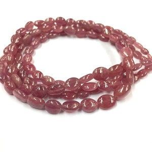 May include: A strand of pink oval-shaped gemstone beads. The beads are strung on a clear thread and are arranged in a circular pattern.