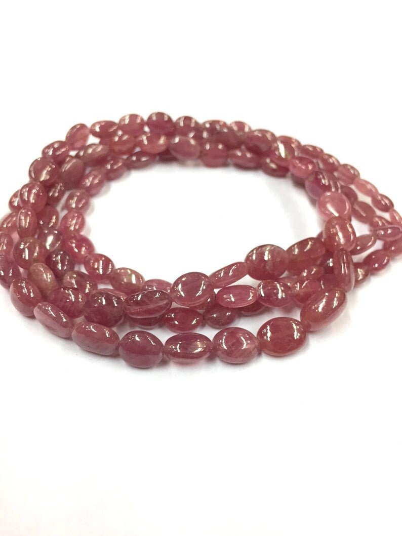 May include: A strand of pink oval-shaped gemstone beads. The beads are strung on a clear thread and are arranged in a circular pattern.