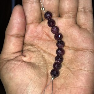 May include: A strand of dark purple gemstone beads with silver metal clasps. The beads are round and faceted.