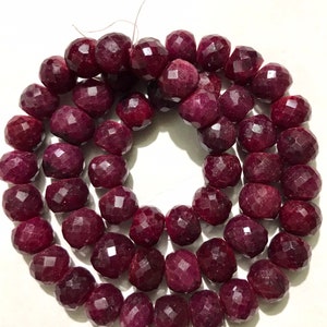 May include: A strand of deep red ruby beads, each bead is faceted and round, the beads are strung on a clear thread.