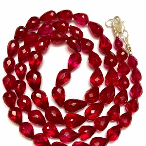 Può includere: Una collana di perle di pietre preziose rosso scuro, ogni perla è sfaccettata e a forma di lacrima. Le perle sono infilate su una catena d'argento con una chiusura d'argento.