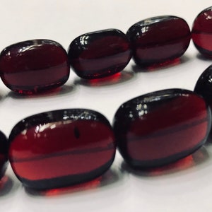 Puede incluir: Una hebra de cuentas ovaladas de color rojo oscuro. Las cuentas son de vidrio y tienen un acabado brillante.