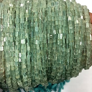 Könnte beinhalten: Eine Strähne aus hellgrünen Aquamarinperlen, jede Perle ist facettiert und hat eine quadratische Form.