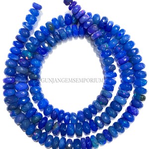 May include: A strand of blue opal beads with a faceted, barrel shape. The beads are strung on a clear thread and are approximately 10mm in diameter. The beads have a slight iridescent quality.
