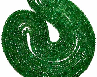 Könnte beinhalten: Eine Kette aus smaragdgrünen Edelsteinperlen, auf einer goldenen Schnur aufgefädelt. Die Perlen sind facettiert und haben eine leicht unregelmäßige Form. Die Kette ist zu einem lockeren Kreis gewickelt.