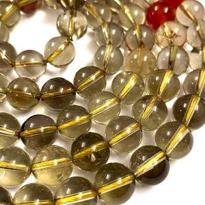 May include: A strand of smoky quartz beads with gold accents. The beads are round and translucent, with a light brown color. The gold accents are thin lines that run around the circumference of the beads.