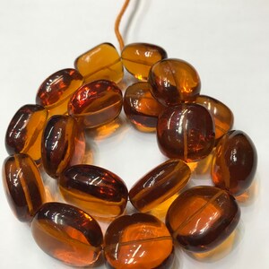 May include: A strand of amber-colored glass beads, each bead is oval-shaped and has a smooth, polished finish.