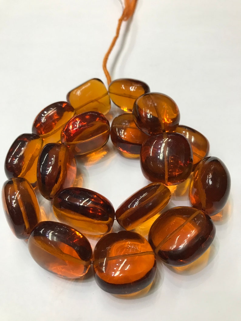 May include: A strand of amber-colored glass beads, each bead is oval-shaped and has a smooth, polished finish.