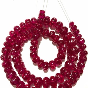 May include: A strand of deep red, faceted, pumpkin-shaped beads. The beads are strung on a thin wire and are arranged in a circular pattern.