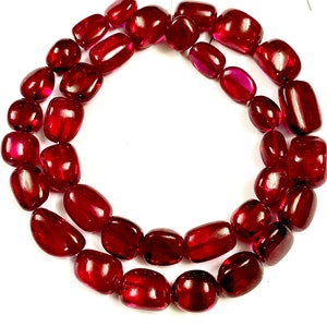 Puede incluir: Una hebra de cuentas de piedras preciosas de color rojo intenso, cada cuenta tiene una forma rectangular redondeada y lisa.