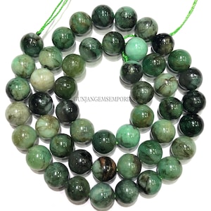 以下が含まれることがあります： 濃い緑と茶色のインクルージョンが入った丸い緑のエメラルドビーズのストランド。ビーズは緑色の糸に通されています。