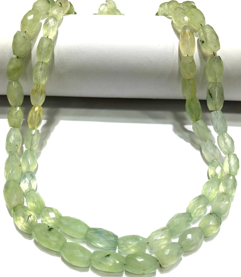 May include: A strand of light green gemstone beads, likely aventurine, with a faceted oval shape. The beads are strung on a clear thread and are arranged in a double row.