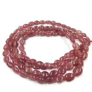 May include: A strand of pink oval-shaped gemstone beads. The beads are smooth and polished, and they have a slightly translucent appearance.