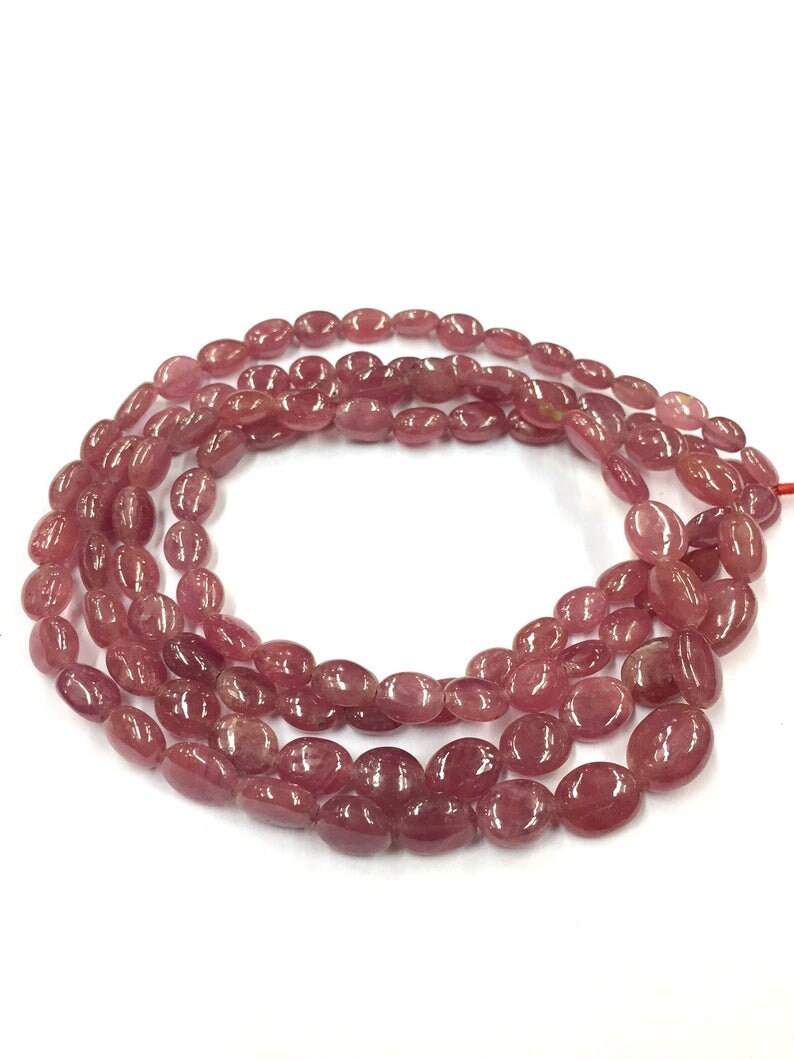 May include: A strand of pink oval-shaped gemstone beads. The beads are smooth and polished, and they have a slightly translucent appearance.
