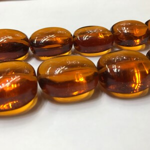 May include: A strand of amber glass beads, each bead is oval shaped and has a smooth, polished finish.
