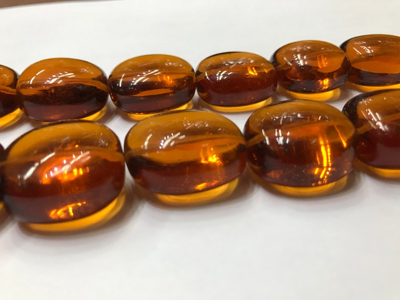 May include: A strand of amber glass beads, each bead is oval shaped and has a smooth, polished finish.