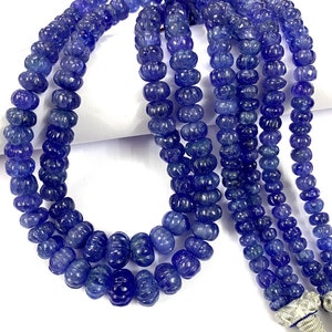 May include: A strand of blue gemstone beads, each bead is carved with a textured design. The beads are strung on a cord and have a silver clasp.