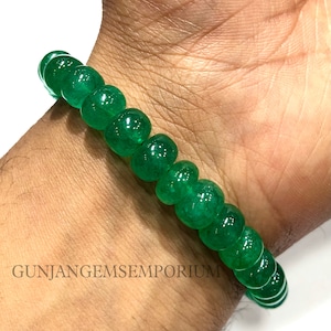Op de afbeelding: Een groene smaragdstenen armband met ronde kralen. De armband zit om een pols.