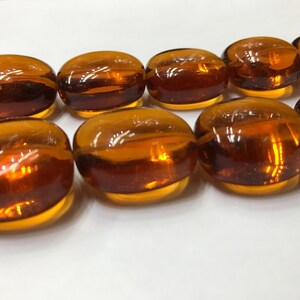 May include: A strand of amber glass beads, each bead is oval shaped and has a smooth, glossy finish.