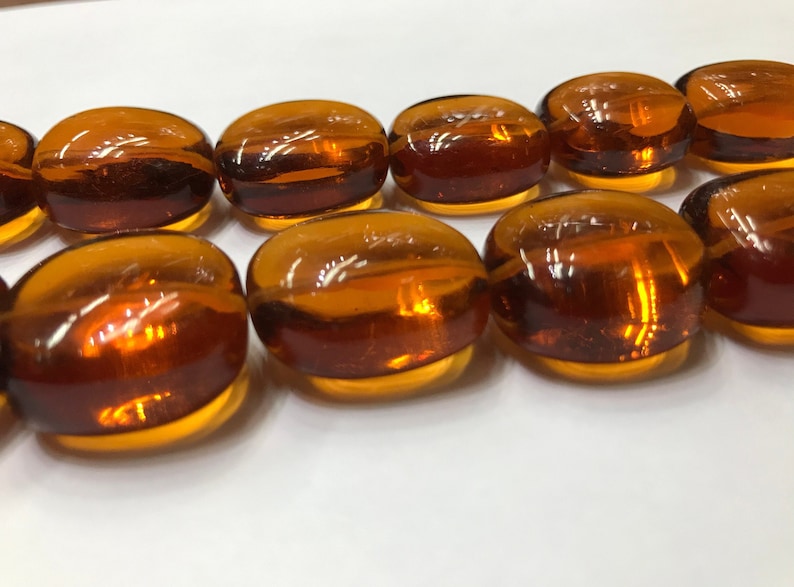 May include: A strand of amber glass beads, each bead is oval shaped and has a smooth, glossy finish.
