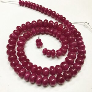 May include: A strand of deep red ruby beads, each bead is round and slightly elongated. The beads are strung on a thin wire and are arranged in a spiral pattern.