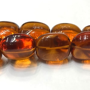 May include: A strand of amber-colored oval-shaped beads. The beads are translucent and have a glossy finish.