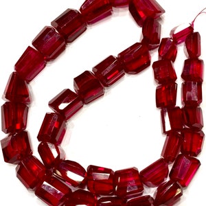 Può includere: Una collana di perline di pietra preziosa sfaccettata rosso scuro. Le perline sono di forma rettangolare e hanno una finitura lucida.