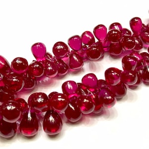 May include: A strand of deep red teardrop-shaped beads. The beads are strung together to form a necklace or bracelet.