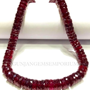 May include: A strand of deep red gemstone beads, likely ruby, with a faceted, barrel-shaped design. The beads are strung on a clear thread and are approximately 10mm in diameter.