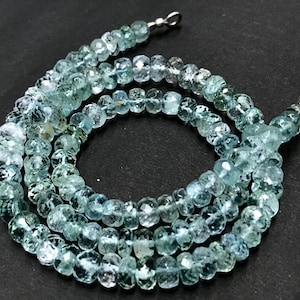 May include: A strand of light blue aquamarine beads, faceted and round, strung on a silver chain. The beads are approximately 4mm in diameter.