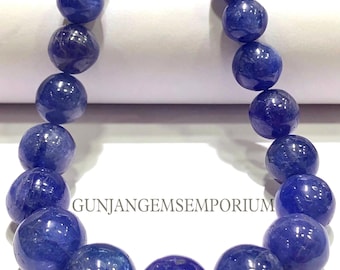 Könnte beinhalten: Eine Kette aus runden, blauen Edelsteinperlen. Die Perlen sind alle ungefähr gleich groß und auf einem durchsichtigen Faden aufgefädelt. Die Perlen sind kreisförmig angeordnet und die Kette liegt auf einer weißen Oberfläche. Der Text "GUNJANGEMSEMPORIUM" ist auf dem Bild zu sehen.