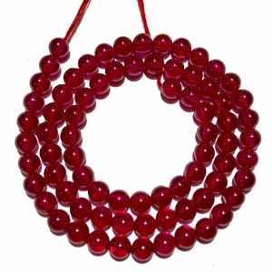Może przedstawiać: Szereg głębokoczerwonych koralików z kamieni szlachetnych, nawleczonych na czerwony sznurek. Koraliki są okrągłe i gładkie, z błyszczącym wykończeniem.