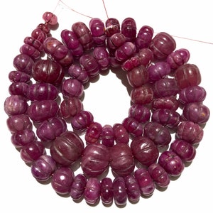 Op de afbeelding: Een streng roze robijn kralen, elke kraal is gesneden met een textuurontwerp. De kralen zijn geregen op een dunne draad en zijn klaar om tot een ketting of armband te worden gemaakt.
