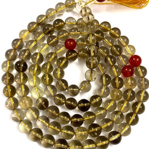 May include: A 108-bead mala necklace made of smoky quartz with gold accents. The beads are round and have a translucent appearance. The necklace is finished with a tassel.